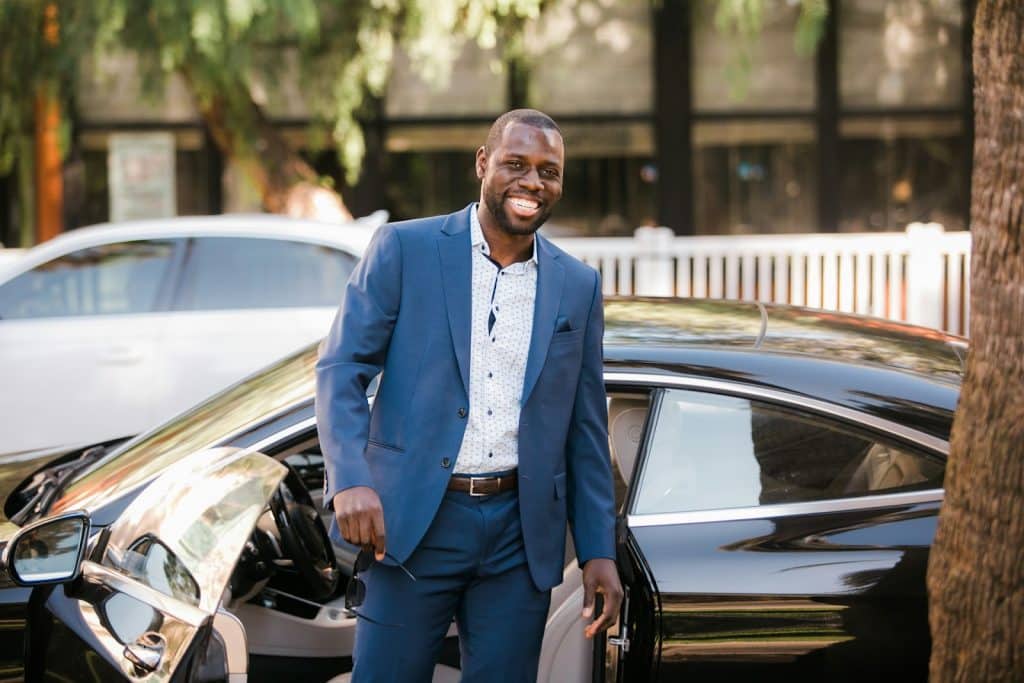 The man in a blue suit is standing beside his car.