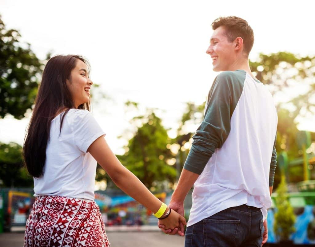 The couple is holding hands while walking in an amusement park.
