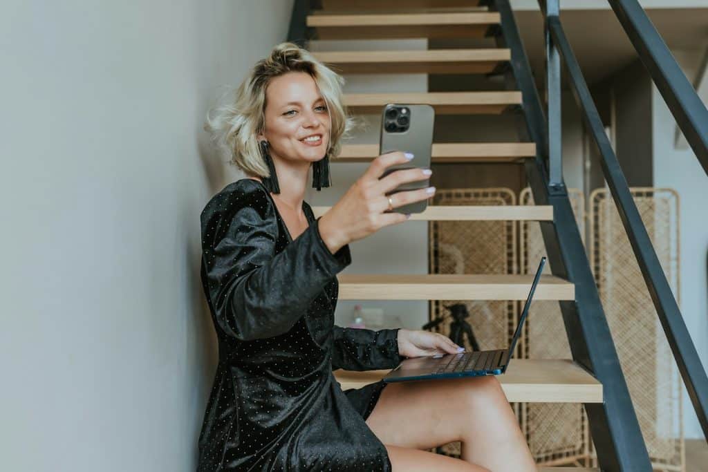 The woman sitting on the stairs is taking a selfie.