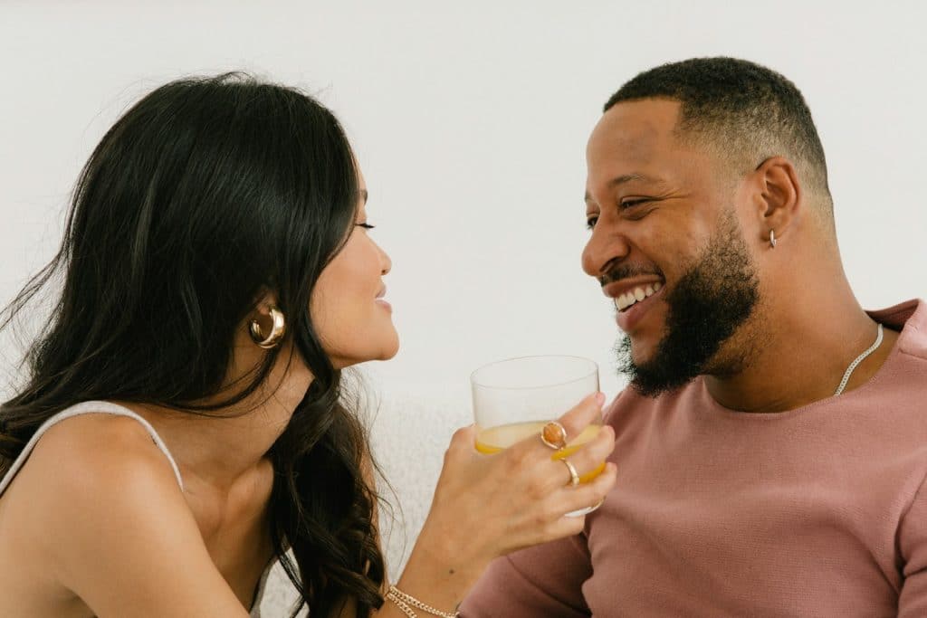 The woman holding a glass is smiling at the man.