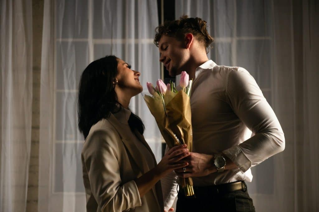 The woman smiles as she receives the flowers from the man.