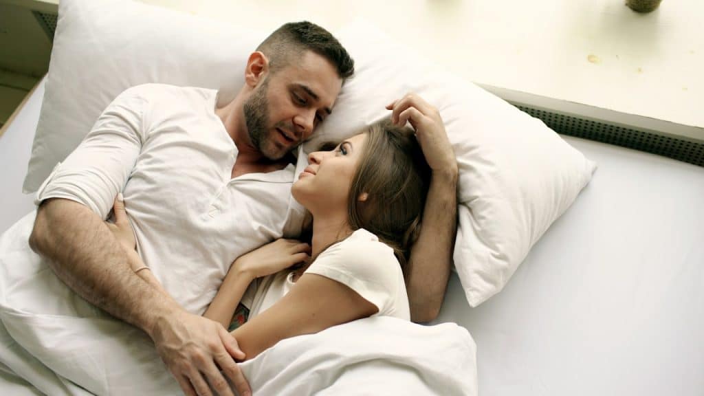 The couple is looking at each other while lying on the bed.