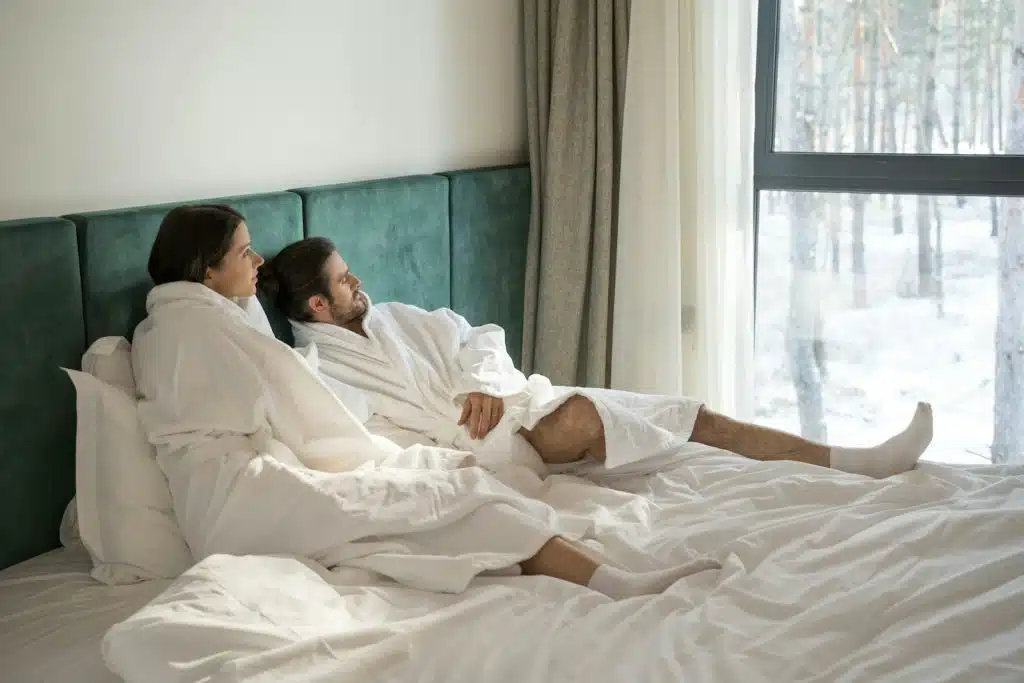 The couple wearing bath robes is looking outside the window.