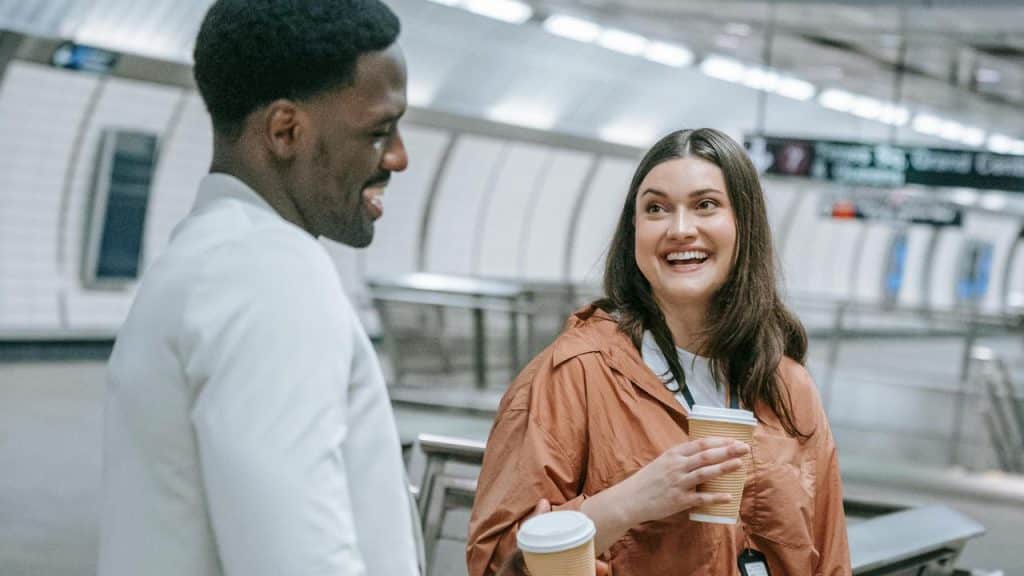 A man and a woman smiling while holding coffee cups.