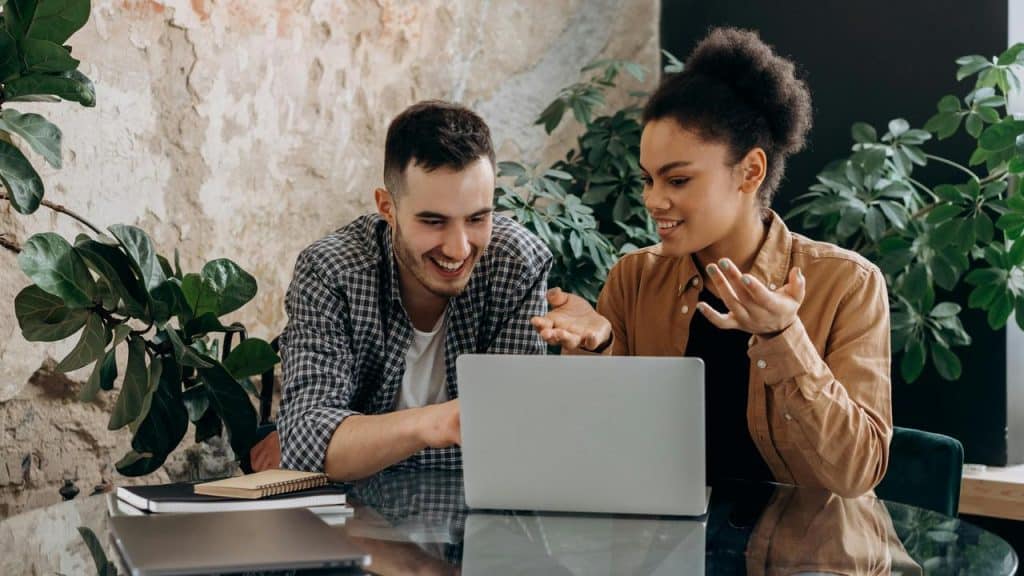 A man and a woman smiling while working on a laptop together.