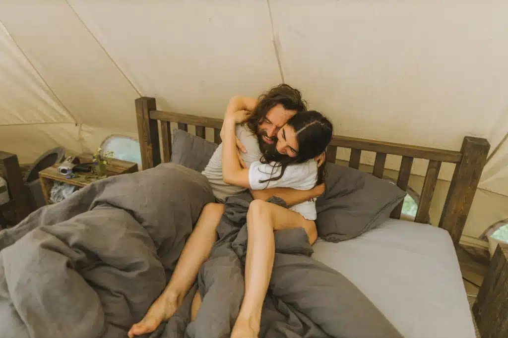 A man and woman hugging while at the bed