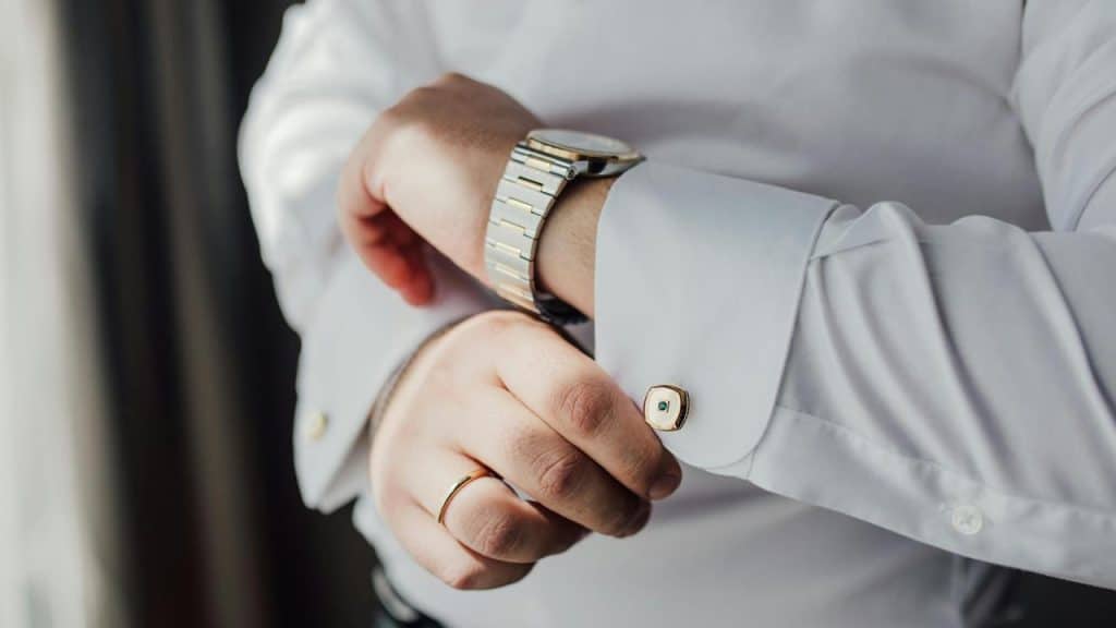 A man adjusting his shirt cuff while wearing a watch.