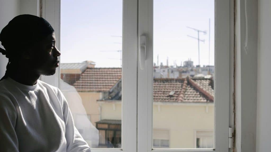 A man in a white shirt sitting by a window and looking outside.