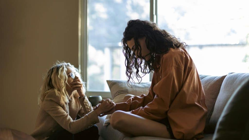 A comforting moment between two women sitting on a couch and holding hands.