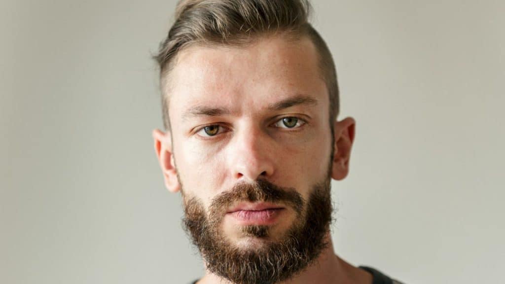 Close-up portrait of a man with a beard, a styled haircut, and heterochromia (different colored eyes).