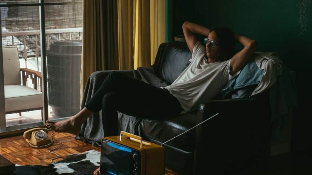 Person wearing a white shirt and sunglasses lounging barefoot on a black couch.