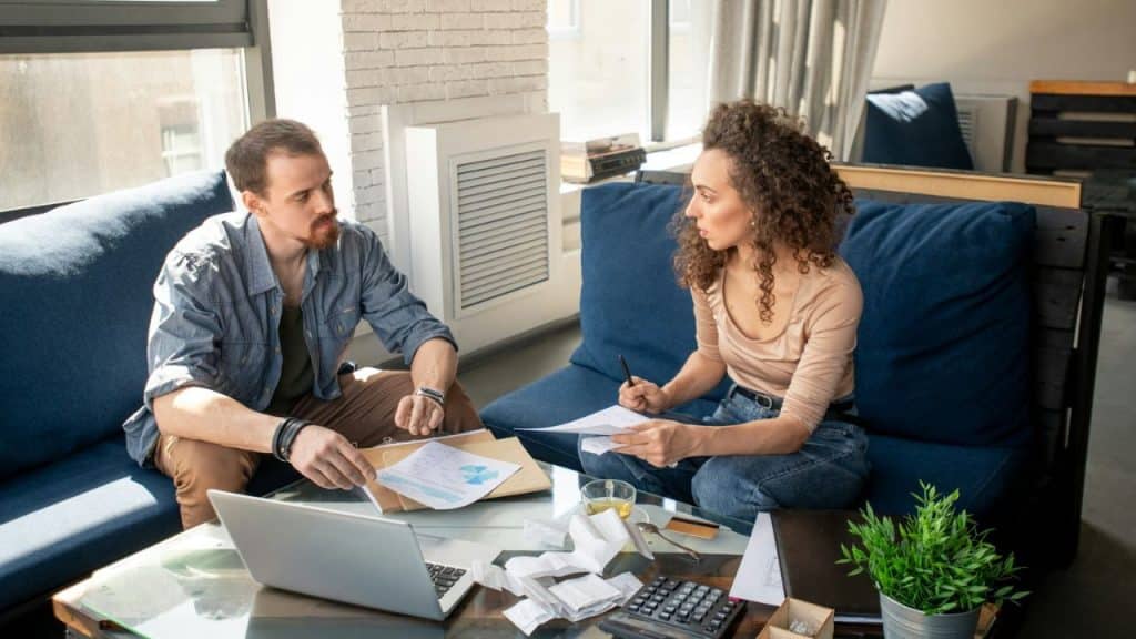 Man and woman discussing paperwork and a laptop while sitting across from each other on a blue couch.