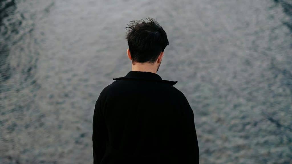 A man standing alone facing the water.