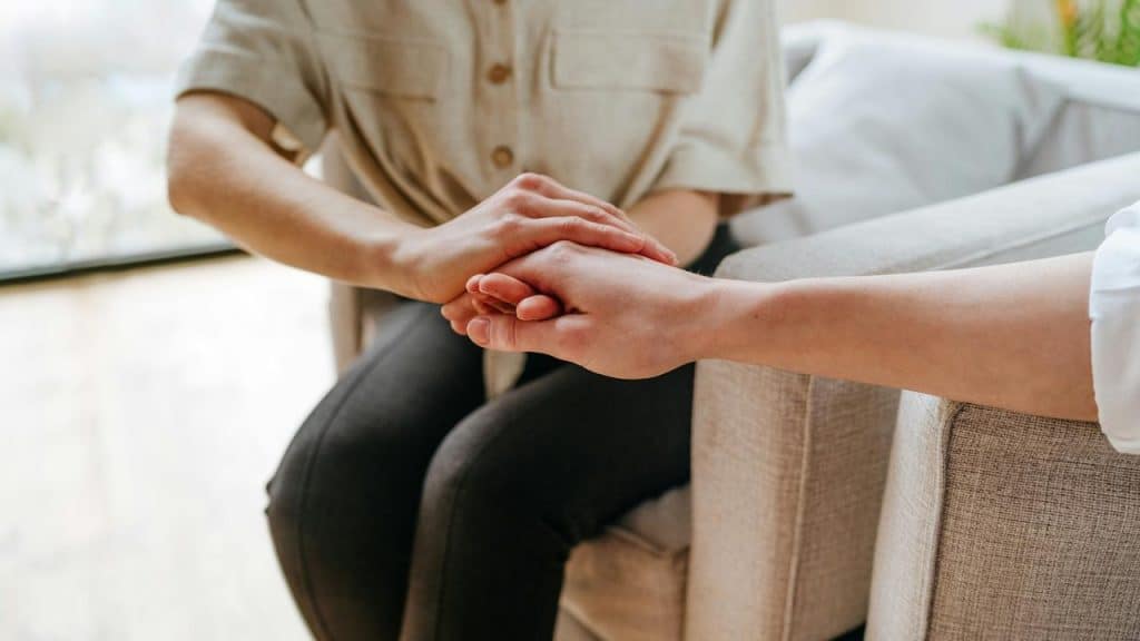 A person gently holding another person’s hand in support.