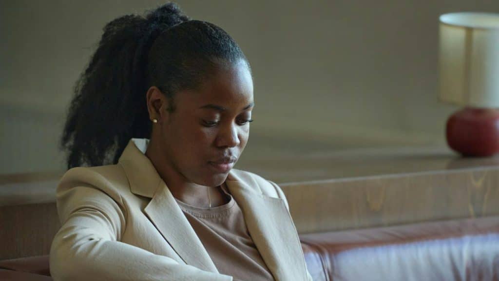 A woman sitting on a couch looking down with a thoughtful expression.