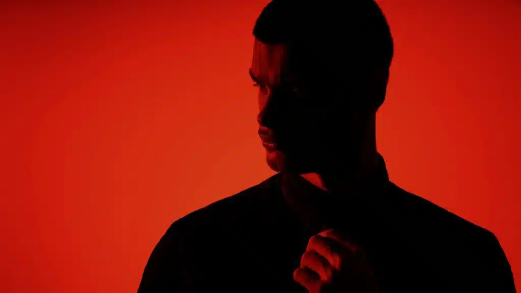 A man looking to the side while shrouded in shadow against a red background.