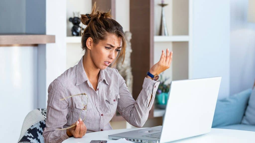 A woman looking at her laptop with an exasperated expression and gesturing with her hand.