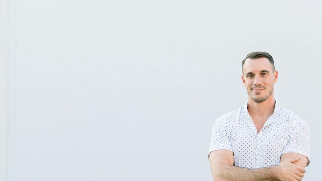 A man standing with his arms crossed in front of a white wall.