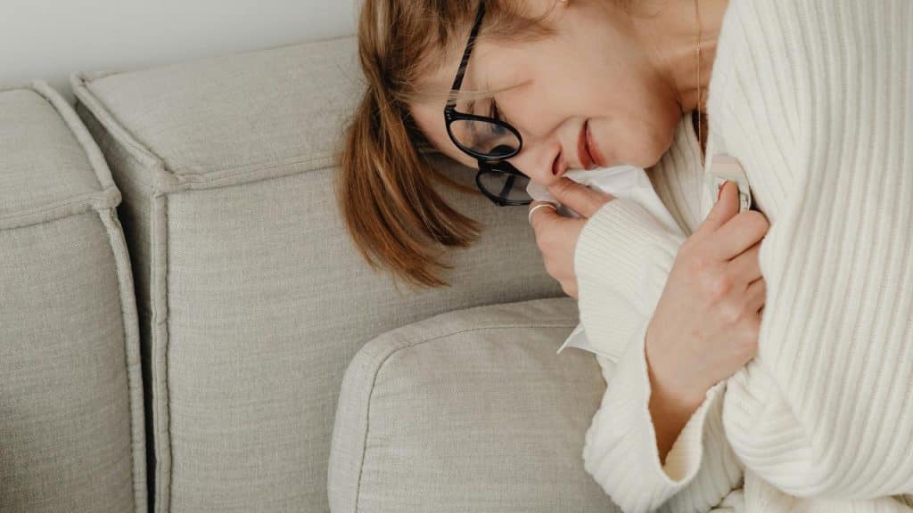 A woman lying on a couch holding a tissue and looking emotional.