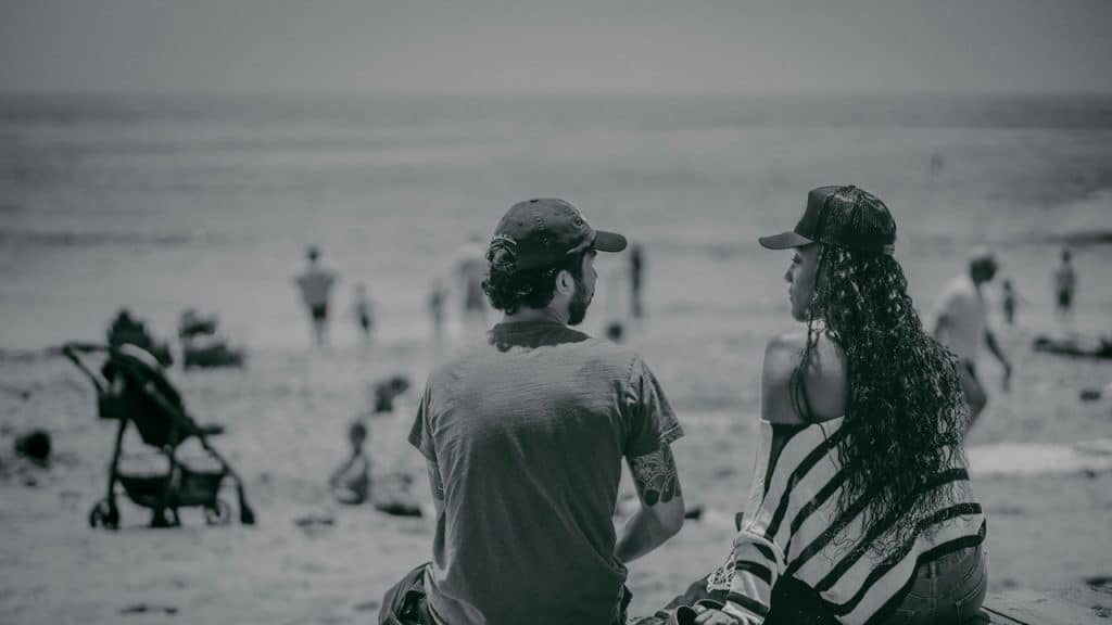 A man and a woman sitting on a pier looking at the beach