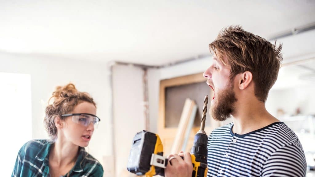 A man and a woman working with an electric drill in the carpenter workroom.