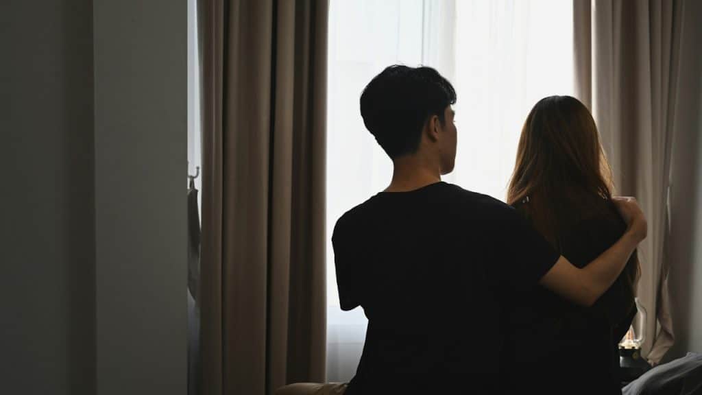 Young man embracing his wife while sitting in the bedroom.