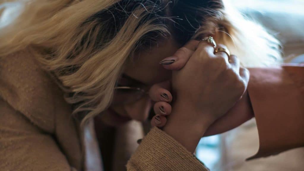 A woman bowing her head while holding someone’s hand in support.