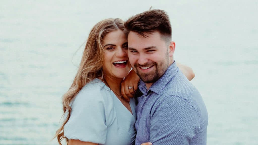 A couple hugging in front of the ocean and smiling.