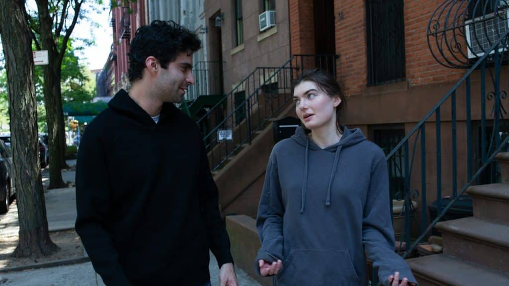 A woman shrugging while a man stands next to her on a sidewalk.