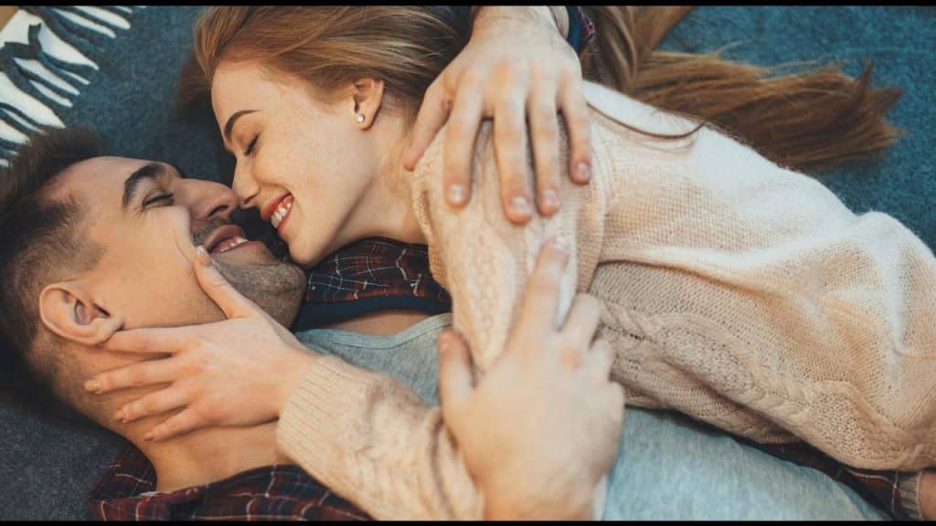 A couple lying on a blanket smiling and embracing each other.