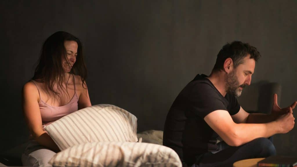 A couple sitting on a bed with the woman crying while her man refuses to look at her.