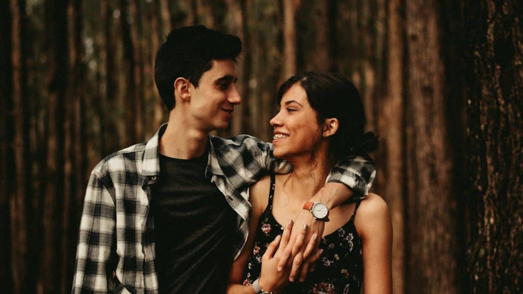 A couple looking at each other and smiling with the man placing his arm around the woman’s shoulder.