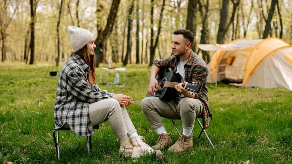 A couple on a camping trip where the man is playing a guitar for the woman.