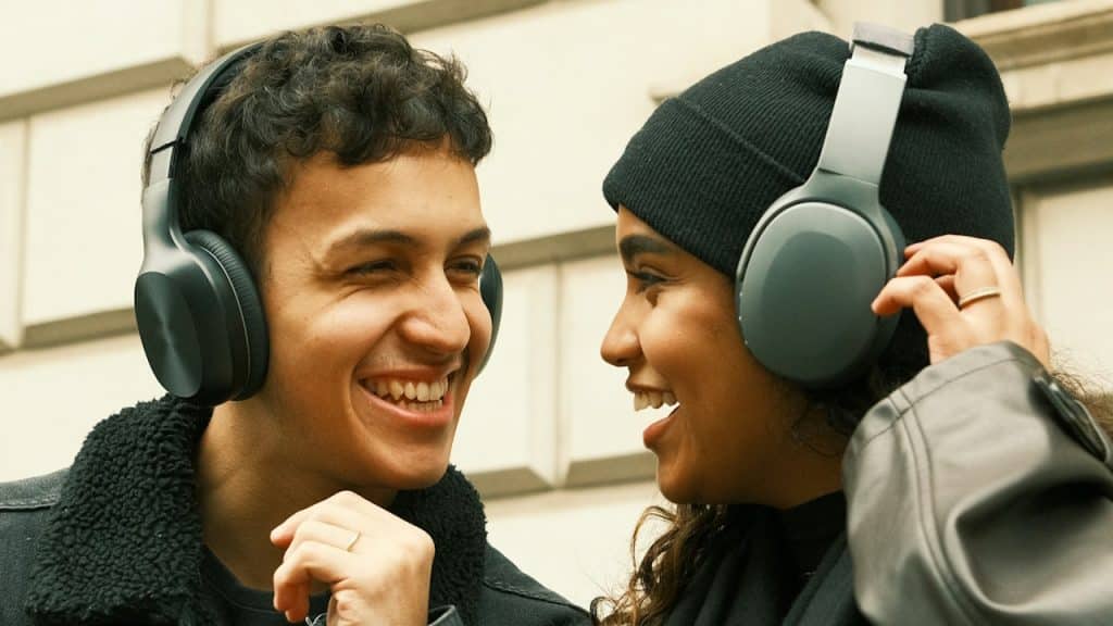 A couple wearing headphones and listening to music while smiling at each other.