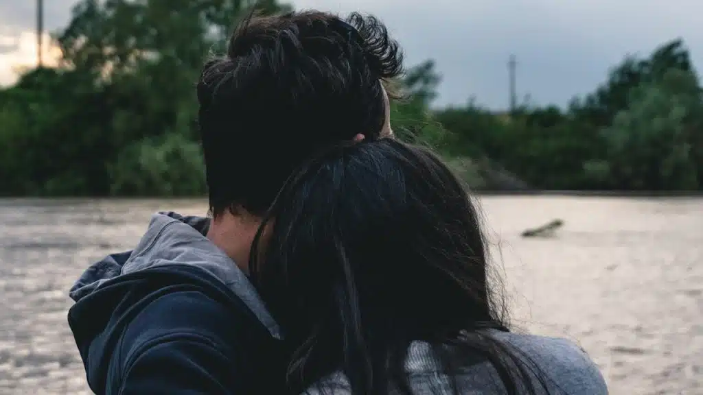 A couple hugging and looking outwards at a lake.