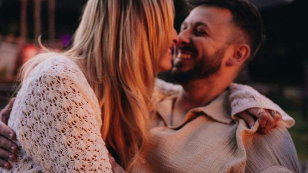 A couple smiling and leaning in for a kiss outdoors.