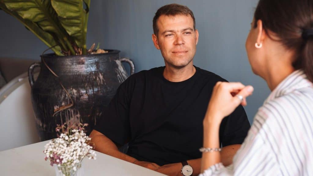 A man and woman sitting at a table having a conversation indoors.