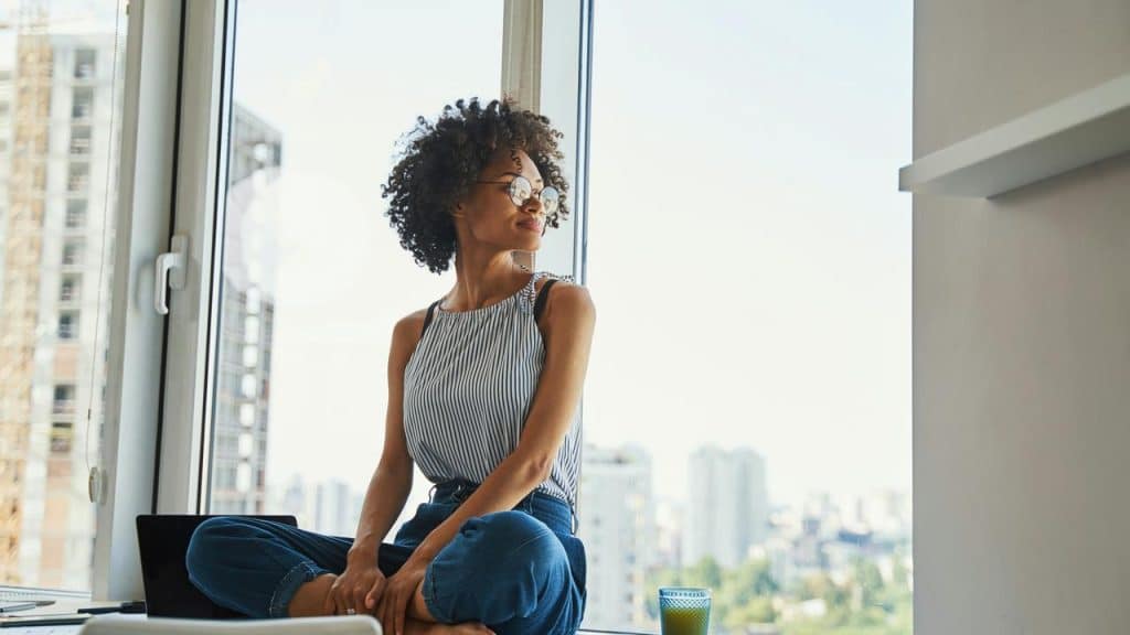A woman sitting by a window looking outside with a relaxed expression.