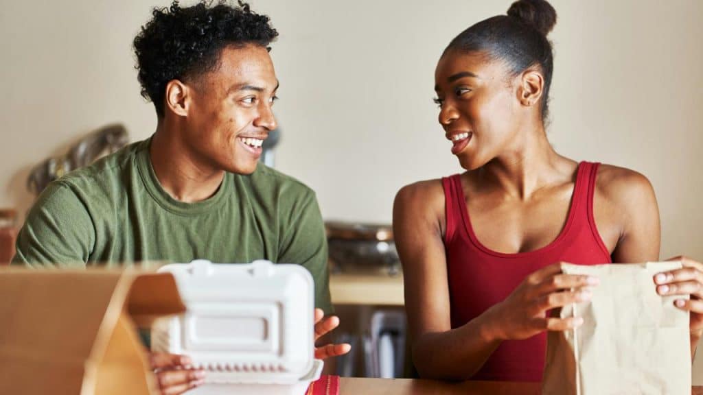 A couple smiling and talking while unpacking food containers.