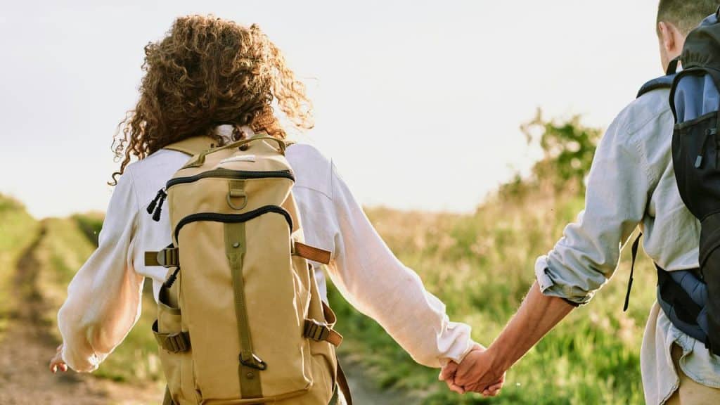 A couple holding hands while walking on a trail with backpacks.
