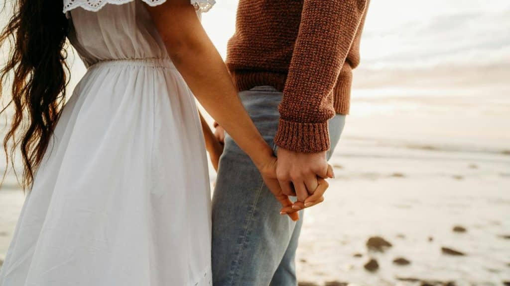 A couple holding hands while standing on the beach.