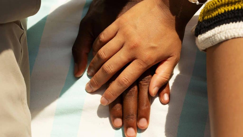 A close-up of two people’s hands resting together in a comforting gesture.