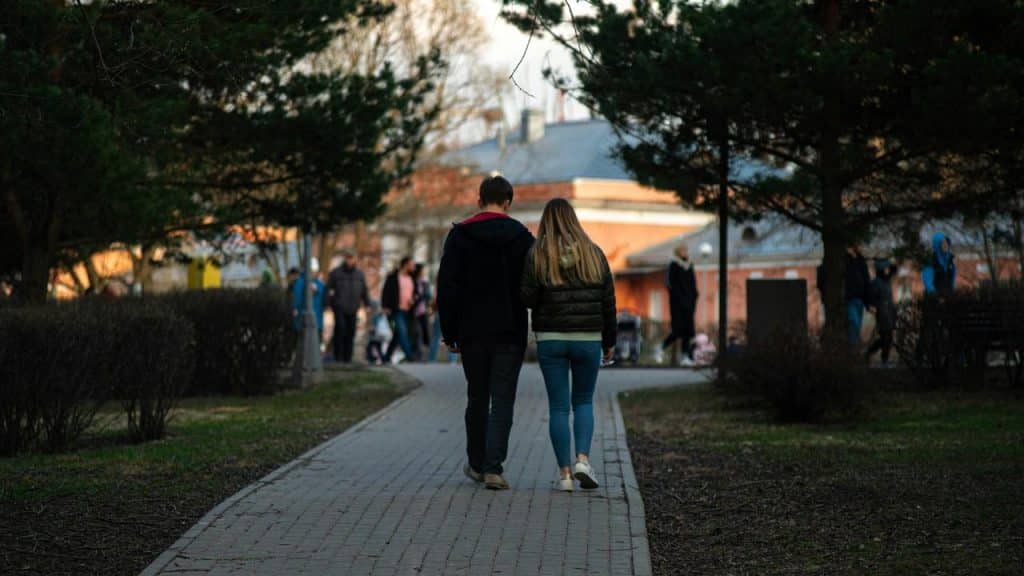 A couple walking together down a park path surrounded by trees.