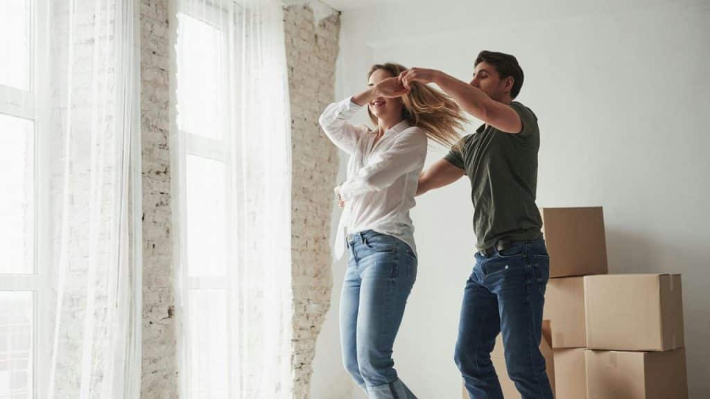 A couple dancing together in a bright room with moving boxes.