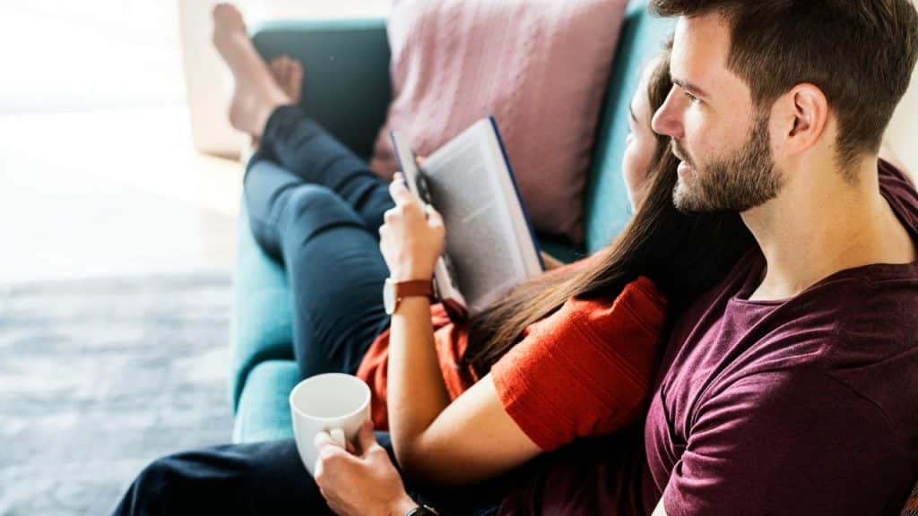 A couple relaxing on a couch, reading and sharing a quiet moment together.