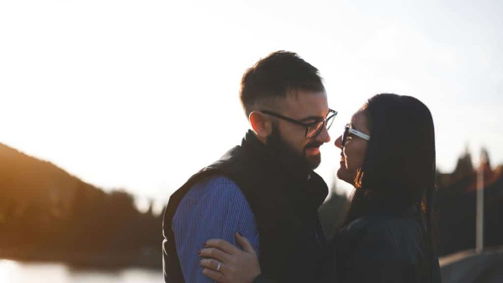 A couple smiling and looking at each other outdoors at sunset.