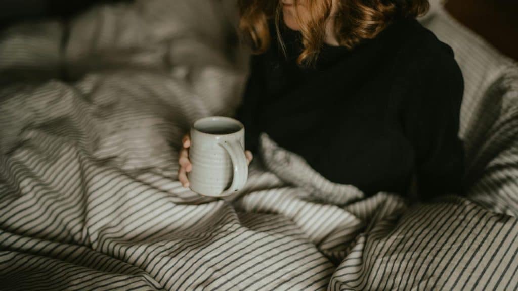 A woman sitting in bed holding a mug.
