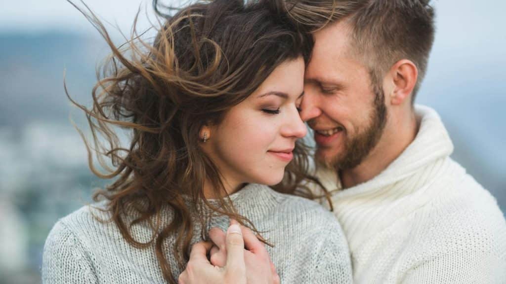 A couple embracing each other outdoors with the wind blowing their hair.