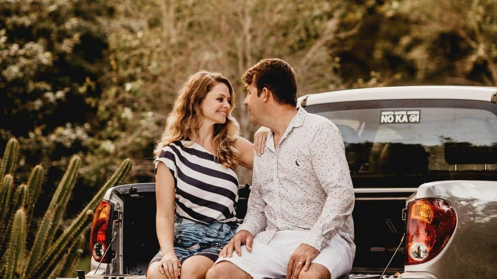 A couple sitting on the back of a pickup truck smiling at each other.