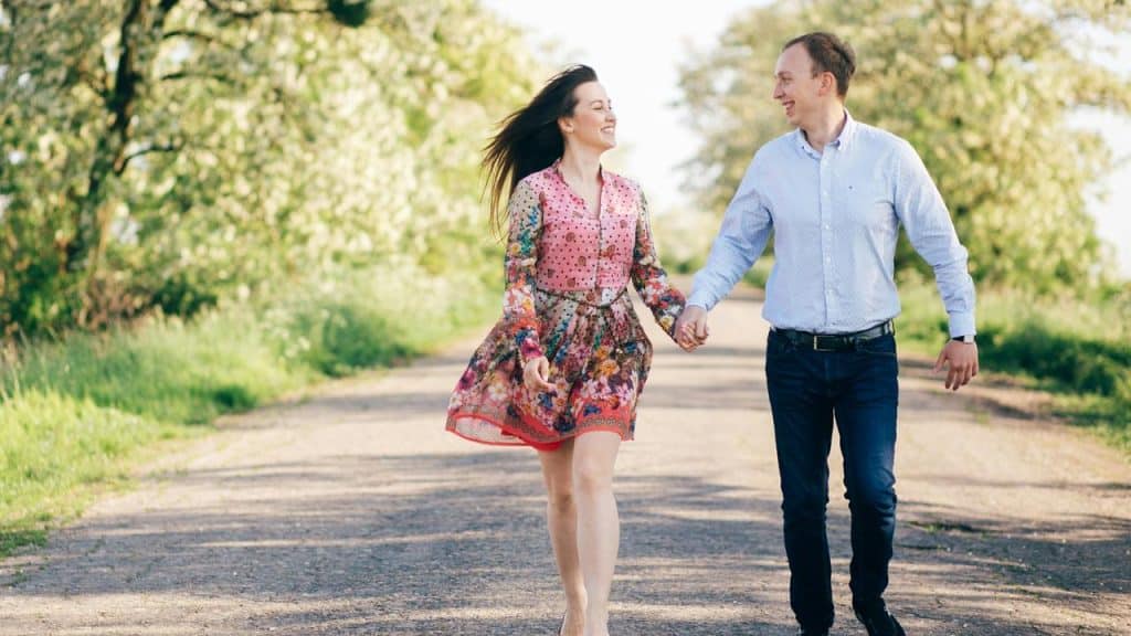 A couple holding hands while walking on a tree-lined path.